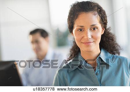 Portrait of businesswoman in office with male executive working in background View Large Photo Image Stock Photo - Portrait of businesswoman in office with male executive working in background. Fotosearch