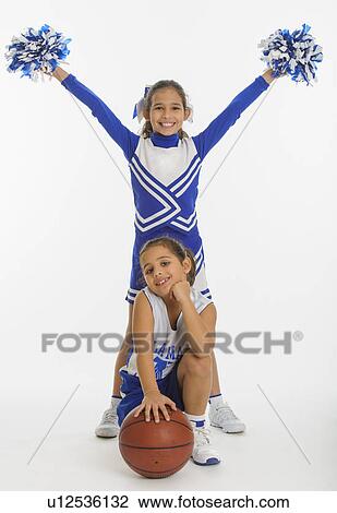 Stock Image - Portrait of cheerleaders (8-9 years) ( 10-11 years) holding pom-pom and ball. Fotosearch