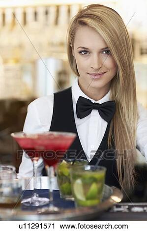 Stock Image - Portrait of female bartender holding tray with cocktails. Fotosearch