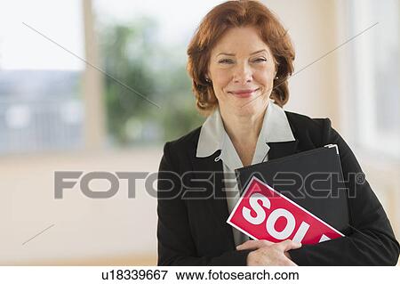 Stock Photo - Portrait of female real estate agent holding sold sign. Fotosearch