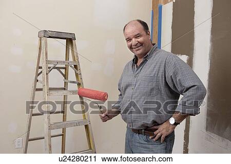 Stock Image - Portrait of man holding paint roller. Fotosearch