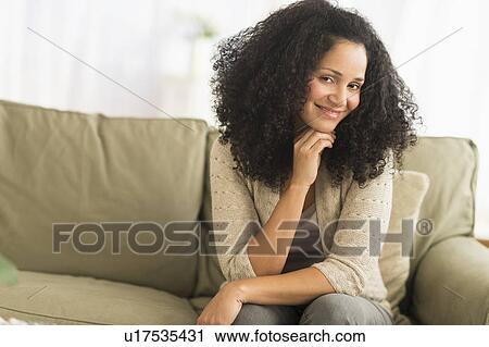 Stock Image - Portrait of mid adult woman sitting on sofa. Fotosearch
