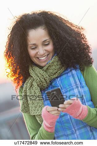 Stock Photo - Portrait of mid adult woman using mobile phone at sunset. Fotosearch
