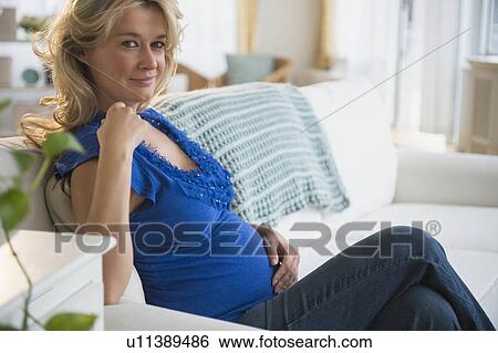 Stock Photograph - Portrait of pregnant woman sitting on sofa. Fotosearch