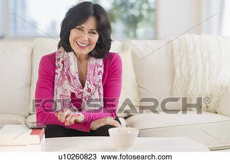Stock Image - Portrait of senior woman sitting in living room. Fotosearch