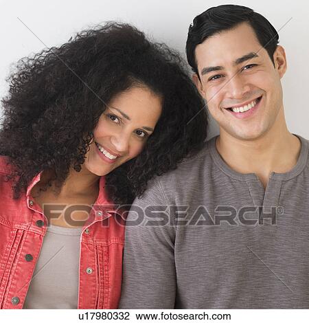 Stock Image - Portrait of smiling couple standing against white wall. Fotosearch