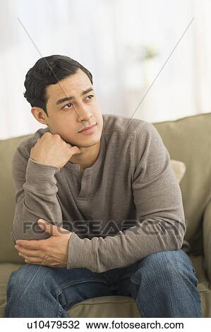 Stock Image - Portrait of smiling man sitting on sofa. Fotosearch