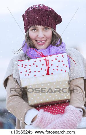Stock Photography - Portrait of young woman carrying stack of Christmas presents. Fotosearch
