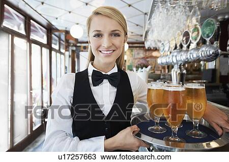 Stock Image - Portrait of young woman holding tray with beer glasses. Fotosearch