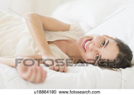 Stock Image - Portrait of young woman lying in bed. Fotosearch
