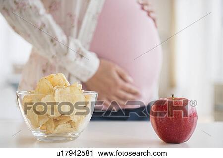Pregnant woman choosing between apple and chips View Large Photo Image Stock Image - Pregnant woman choosing between apple and chips. Fotosearch