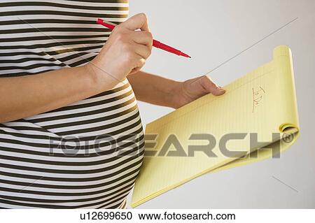 Stock Image - Pregnant woman holding pencil and notebook. Fotosearch