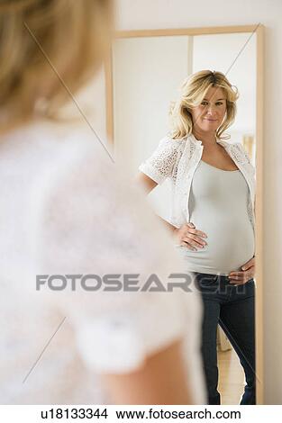 Picture - Pregnant woman looking in mirror. Fotosearch