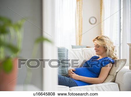 Stock Photo - Pregnant woman sitting on sofa. Fotosearch
