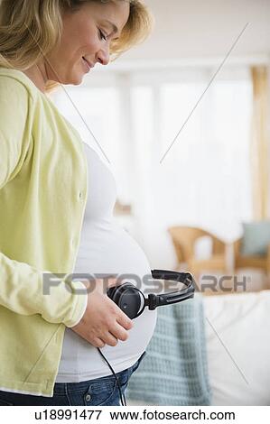 Stock Photo - Pregnant woman with headphones on belly. Fotosearch