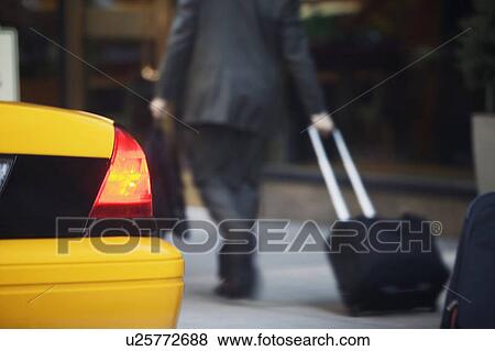 Rear view of businessman pulling suitcase by yellow taxi View Large Photo Image Stock Photo - Rear view of businessman pulling suitcase by yellow taxi. Fotosearch