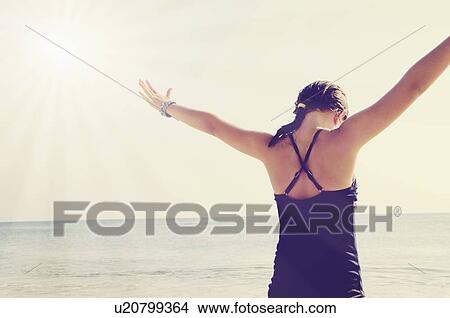 Picture - Rear view of girl (8-9) standing with arms raised. Fotosearch