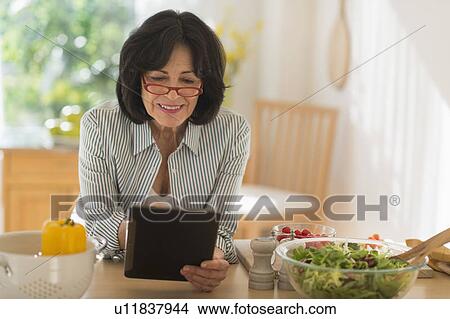 Picture - Senior woman holding digital tablet while preparing salad . Fotosearch