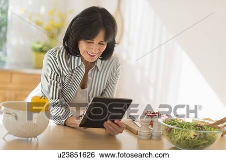 Stock Photograph - Senior woman holding digital tablet while preparing salad . Fotosearch