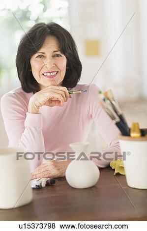 Stock Photo - Senior woman painting handmade pottery. Fotosearch