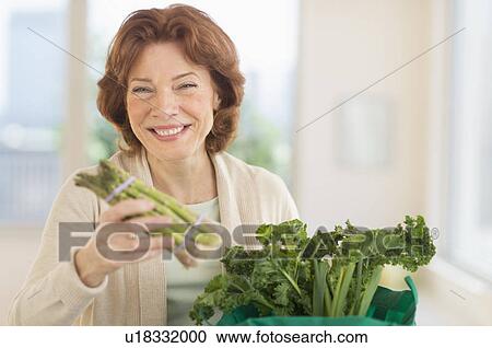Stock Image - Senior woman with groceries in kitchen. Fotosearch