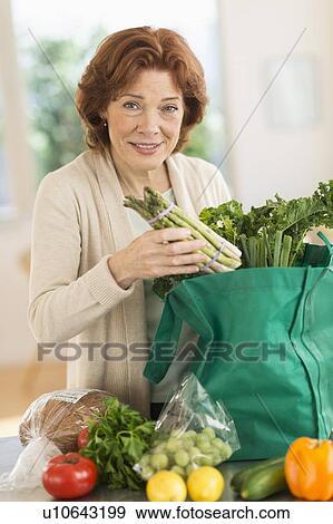 Stock Photo - Senior woman with groceries in kitchen. Fotosearch