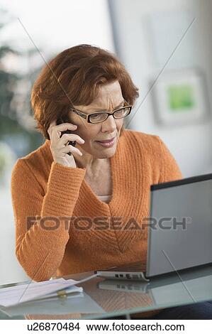 Senior woman working on laptop and talking on cell phone View Large Photo Image Picture - Senior woman working on laptop and talking on cell phone. Fotosearch