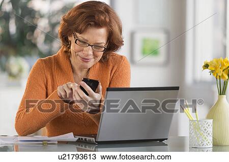 Stock Image - Senior woman working on laptop and text messaging. Fotosearch