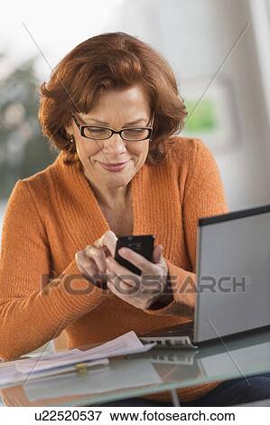 Stock Photo - Senior woman working on laptop and text messaging. Fotosearch