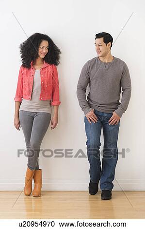 Stock Image - Smiling couple standing against white wall. Fotosearch