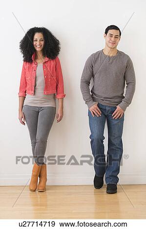 Stock Photo - Smiling couple standing against white wall. Fotosearch