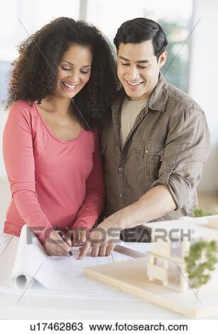 Stock Image - Smiling couple with model home. Fotosearch