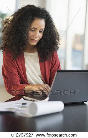 Stock Photo - Smiling mid adult woman doing home finances with laptop. Fotosearch
