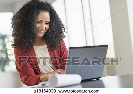 Stock Photo - Smiling mid adult woman doing home finances with laptop. Fotosearch