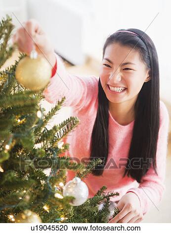 Stock Image - Teenage girl ( 16-17 years) decorating Christmas tree. Fotosearch