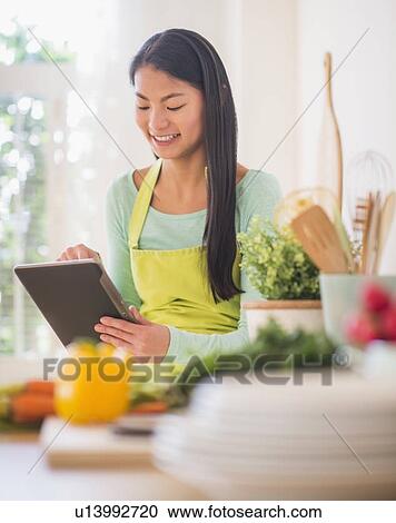 Stock Image - Teenage girl using digital tablet in kitchen. Fotosearch