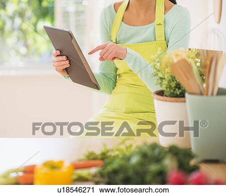 Stock Image - Teenage girl using digital tablet in kitchen. Fotosearch