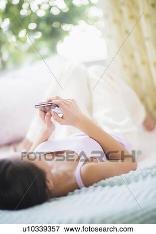 View of Teenage girl (16-17 years) using mobile phone lying on bed View Large Photo Image Stock Photo - View of Teenage girl (16-17 years) using mobile phone lying on bed. Fotosearch