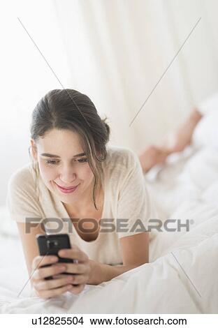 Woman lying in bed and text messaging View Large Photo Image Picture - Woman lying in bed and text messaging. Fotosearch