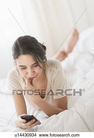 Woman lying in bed and text messaging View Large Photo Image Picture - Woman lying in bed and text messaging. Fotosearch
