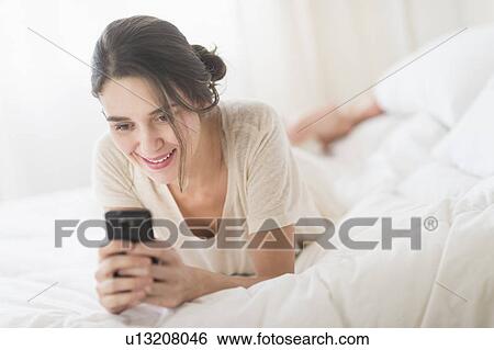 Woman lying in bed and text messaging View Large Photo Image Stock Photograph - Woman lying in bed and text messaging. Fotosearch