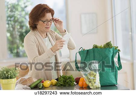 Stock Image - Woman reading shopping list in kitchen. Fotosearch