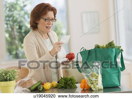 Stock Image - Woman reading shopping list in kitchen. Fotosearch
