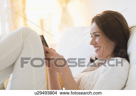 Picture - Woman sitting on sofa and texting. Fotosearch