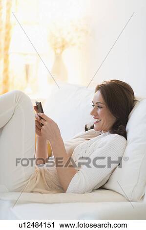 Stock Image - Woman sitting on sofa and texting. Fotosearch