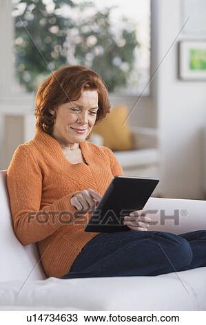 Stock Image - Woman sitting on sofa using digital tablet. Fotosearch