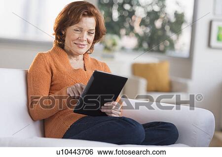Woman sitting on sofa using digital tablet View Large Photo Image Stock Photograph - Woman sitting on sofa using digital tablet. Fotosearch