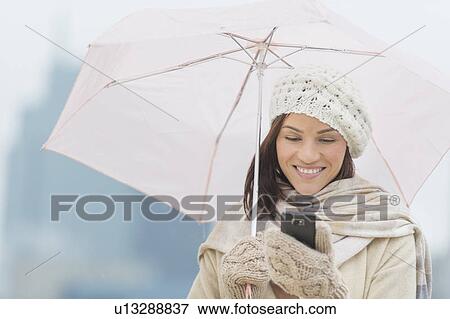 Stock Photo - Woman with umbrella using phone. Fotosearch