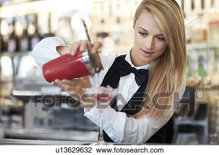 Stock Image - Young female bartender pouring cocktail . Fotosearch
