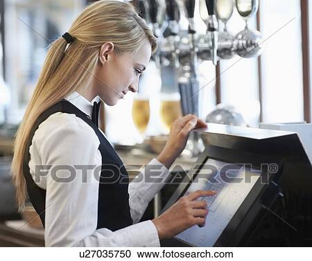 Stock Image - Young waitress using computer at restaurant counter. Fotosearch